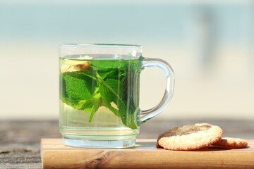 Peppermint tea with green leaves and cookies in front of a beach