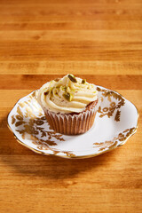 Single carrot cake cupcake served on a white plate with ornate gold details on a wooden surface