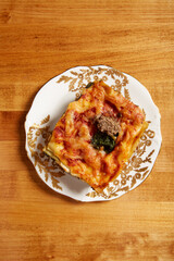 Top view of spinach and mushroom lasagna served on a white plate with gold ornate details