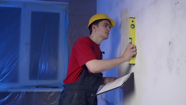 The builder is measuring something, he is wearing construction clothes