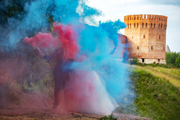 the bride and groom are holding checkers with colored smoke in their hands. a fun wedding walk in summer against the background of a medieval castle. joy and fun with checkers for special fog effects