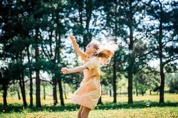 Little baby girl playing in nature. Jumps and runs after soap bubbles, active lifestyle in the park