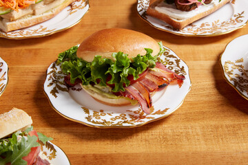 An assortment of sandwiches featuring BLT sandwich served on an white ornate plate with gold details on a wooden surface