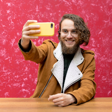 young man sitting at a table taking a selfie with his cell phone 