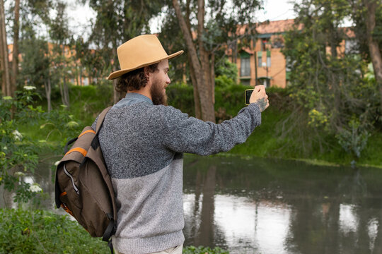 young explorer with hat and backpack taking pictures of the river with his cell phone