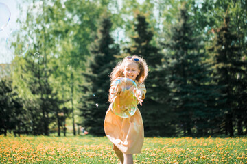 Obraz premium happy emotional sweet girl dancing and playing with soap bubbles enjoying a sunny day in the park.