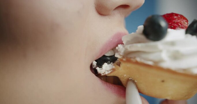 Portrait of young woman eating delicious sweet cake with berries, looking in camera with pleased face. Close-up of female student, happy hungry model tasting cheesecake in studio.