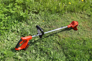 Manual electric trimmer for mowing grass in small volumes in garden and courtyard, on background of green meadow