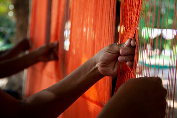 women’s hands weaving a chinchorro with orange nylon thread