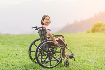 Happy disabled handicapped child sitting in wheelchair on mountain meadow park in sunny day.. International Disability Day.