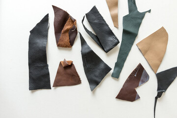 various black, brown, tan, and red-brown leather pieces scattered on a white ground - photographed from above in flat lay composition