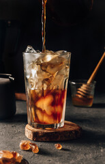 Iced coffee with ice in a tall glass on a dark background.