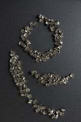 old, worn, recycled square pyramidal leather-craft metallic studs or spikes arranged on a dark grey mat board with low or raking light - photographed from above in a flay lay composition 