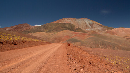 Fototapeta na wymiar The dirt road high in the Andes mountains. Traveling along the route across the arid desert dunes and mountain range. The sand and death valley under a deep blue sky in La Rioja, Argentina.