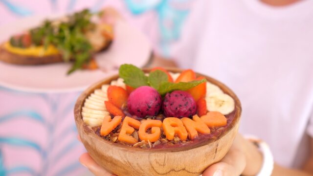 Fruit carving concept. Coconut bowl with smoothie topped with fruits and word vegan carved out of a melon