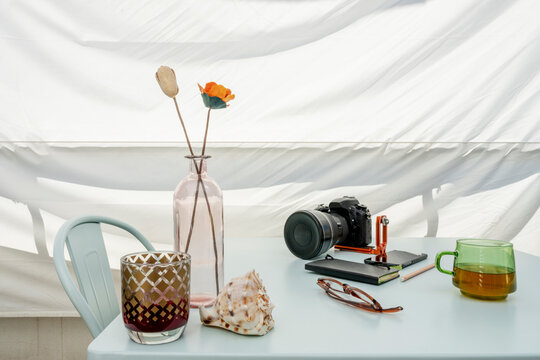 Digital dslr photo camera with ultra wide angle lens on terrace table accompanied by conch shell, vase, cup of tea, glasses