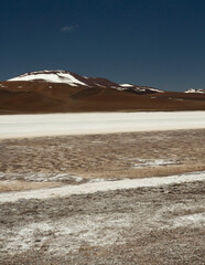 The white desert. Natural salt flats in the cordillera. View of the white salt field and brown mountains under a deep blue sky.