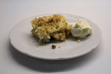Sweet desserts. Apple crumble slice of cake with cream on a white dish in the kitchen table. 