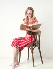 Girl blonde in a red striped dress with glasses and a book on a white background.