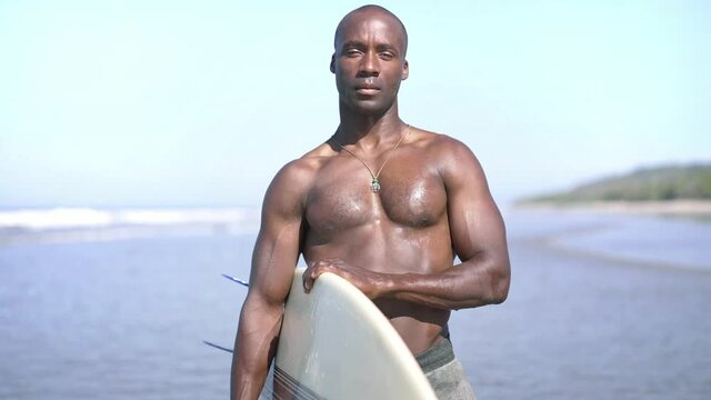 Portrait of confident black african american surfer male standing on beach.  Concept of Fitness Healthy Active Living, Surfing. Summer Vacation. Slow motion.