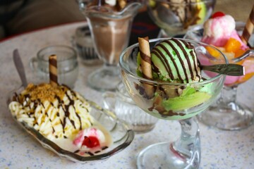 Close up of colorful ice cream on a glass and plate with biscuit, peanut and red cherry on top. Bokeh background. No people.