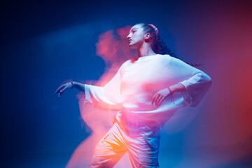 Mixed race young modern girl dancing in colourful neon light. Long exposure. Stylish female moving to rap rhythm