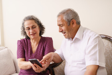 The elderly couple spend time together in their peaceful home. The elderly couple are having fun looking at the phone together. Old people and technology concept.