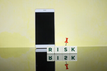 Technology risk concept.  Text on Risk using white cubes reflected on the glass table with a marker pin and smartphone at the back creating a blur effect.  Image contains blur effect 