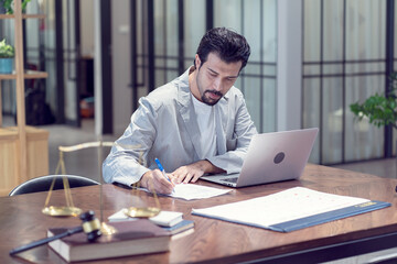 A male lawyer writes a draft contract and examines the documents so that his clients sit and work at a lawyer firm. 