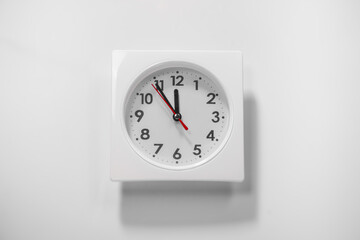 Fototapeta premium It is five to twelve, the clock is ticking. white Watch shows the time 5 before 12. Close up to a wall Clock, with five minutes to twelve o'clock. Time is running out. White background with copy space