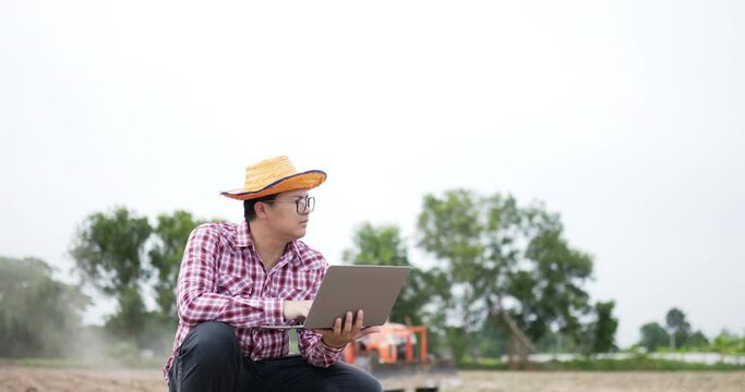 Man squatting in corn field using laptop with tractor