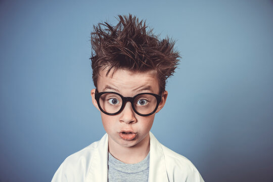 Cool School Boy With Thick Black Glasses Is Dressed As Mad Scientist With White Coat In Front Of Blue Background