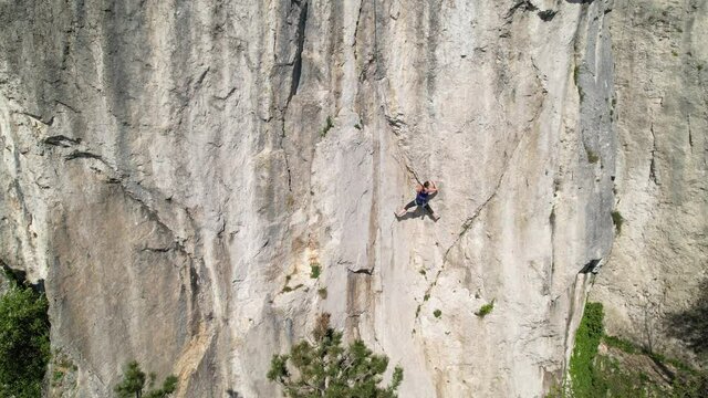 DRONE: Fearless female rock climber learning to top rope looks for a safe hold in the natural wall in Crni Kal. Spectacular drone point of view of an unrecognizable athletic woman learning to climb.
