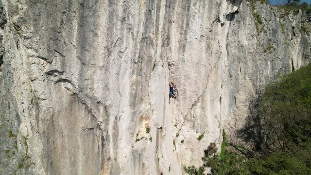 AERIAL: Spectacular drone point of view of an unrecognizable athletic woman learning to climb. Fearless female rock climber learning to top rope looks for a safe hold in the natural wall in Crni Kal.