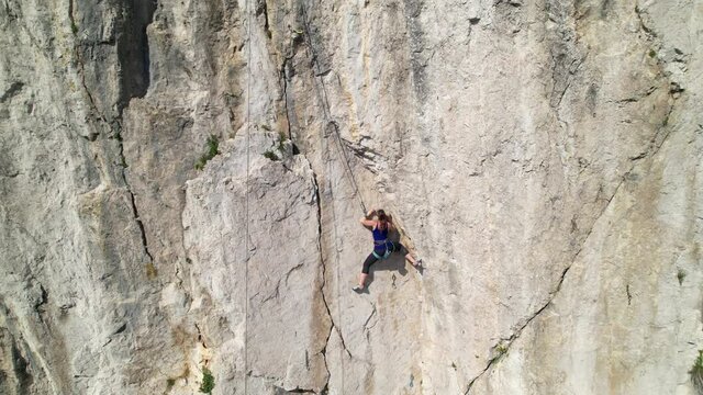 CRNI KAL, SLOVENIA, MAY 2021: AERIAL: Breathtaking flying view of the scenic landscape surrounding an athletic young woman rock climbing in rural Slovenia. Drone point of view of a rock climber in Osp