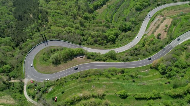 DRONE, TOP DOWN: Flying above tourists on road trip driving through a sharp hairpin turn of a country road near Crni Kal. Cars and motorbikes drive along the scenic switchback road in rural Slovenia.