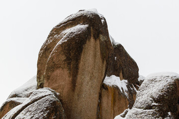 Granite rock is covered with white snow. Brown surface of the stone. Background is the sky. Winter...