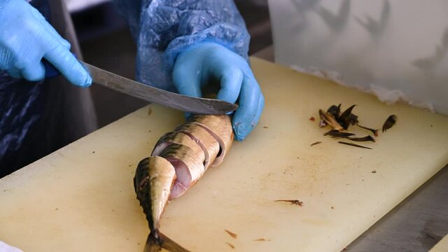 A worker cuts smoked mackerel into pieces with a knife.