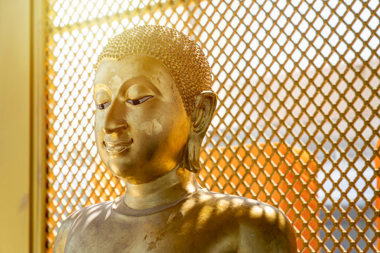 Vintage gold Buddha statue in front of yellow orange grill background with the square pattern light from behind.