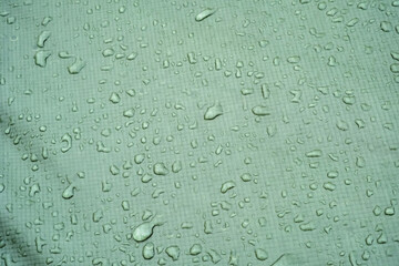 Modern fabric with waterproof repellent coating. Waterproof, rainproof textile concept. Rain drops on green tent.