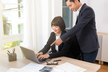 Business man boss pointing finger at computer while woman worker working and typing.