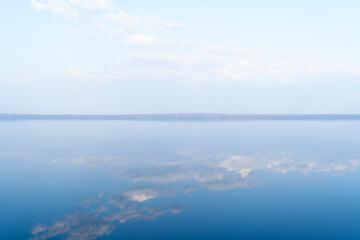 Lake surface with calm water. Smooth water surface with cloud reflections and horizon line. Still calm water texture background.