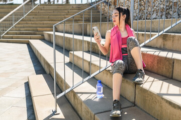 young caucasian sportswoman sitting on concrete steps and using her phone.