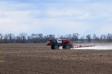 Obraz premium Red tractor with irrigation system watering a field on a cloudy day. agricultural machinery, work in the field. seasonal work. tractor fertilizes the ground. rides in the field, small tractor