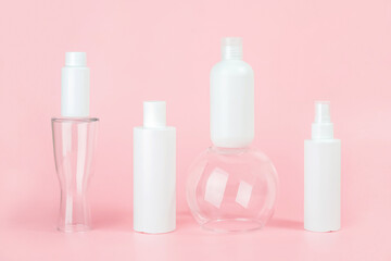 Set of care cosmetic for skin, face, body or hair. White blank cosmetics bottles and tube on glass podiums, pink background. Spa Cosmetic Beauty Concept. Front view Mockup