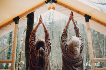 Woman senior and young relaxing at glamping camping tent. Women family elderly mother and young daughter doing yoga and meditation indoor. Modern zen-like vacation lifestyle concept