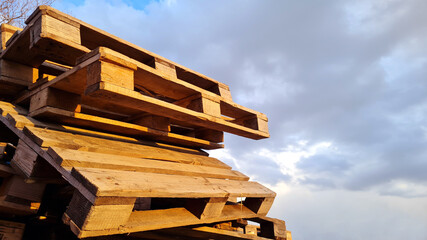 Group of Old Used Wooden pallets is stack outdoors in the warehouse of cargo delivery enterprise on a cloudy sky background.