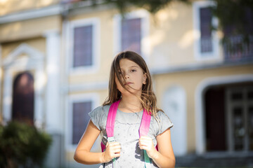  Little girl standing outside with a school bag. Looking at camera.