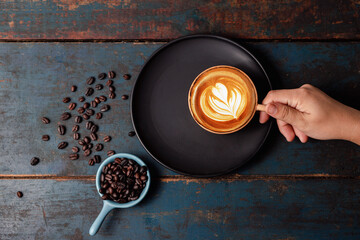 A woman's shot top view, touches a heart shaped hot latte coffee cup on a vintagestyle wooden table.