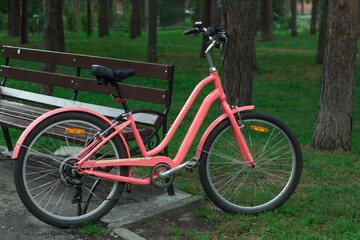 Fototapeta na wymiar Pink women's city bike in a pine Park near a bench.